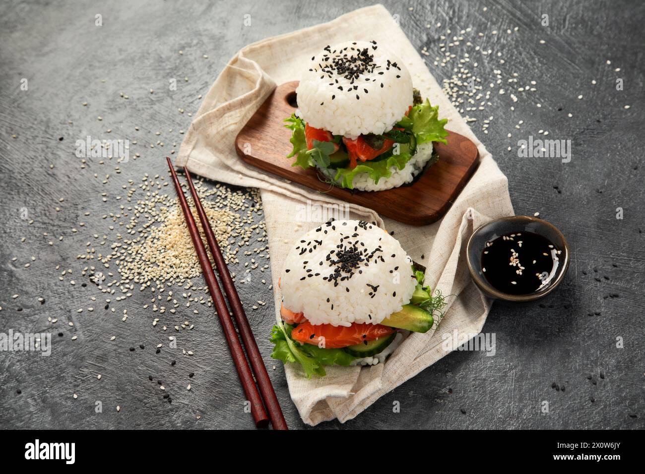 Asiatischer Sushi-Burger, Sojasauce, Essstäbchen auf dunklem Hintergrund. Trendiges Hybrid-Essen. Draufsicht, Kopierraum Stockfoto