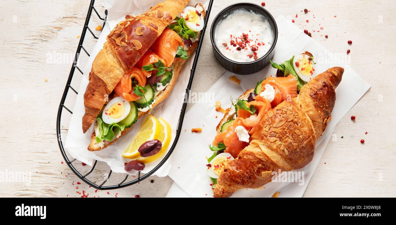 Gesalzenes gesalzenes Frühstück auf hellem Hintergrund. Frisches Lachscroissant mit Frischkäse, Gurke, Ei und Salat. Draufsicht, Banner Stockfoto
