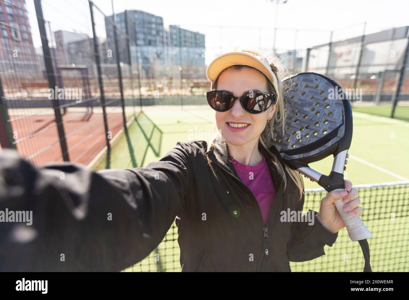 Die sportliche europäische Padel-Tennisspielerin trainiert auf dem Freifeld mit einem Schläger, um den Ball zu schlagen Stockfoto