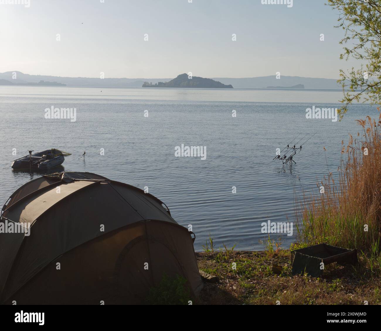 Zelt am Ufer des Bolsenasees mit Angelruten im Freien und einer Insel in der Ferne. Provinz Viterbo, Region Latium, Italien. April 2024 Stockfoto