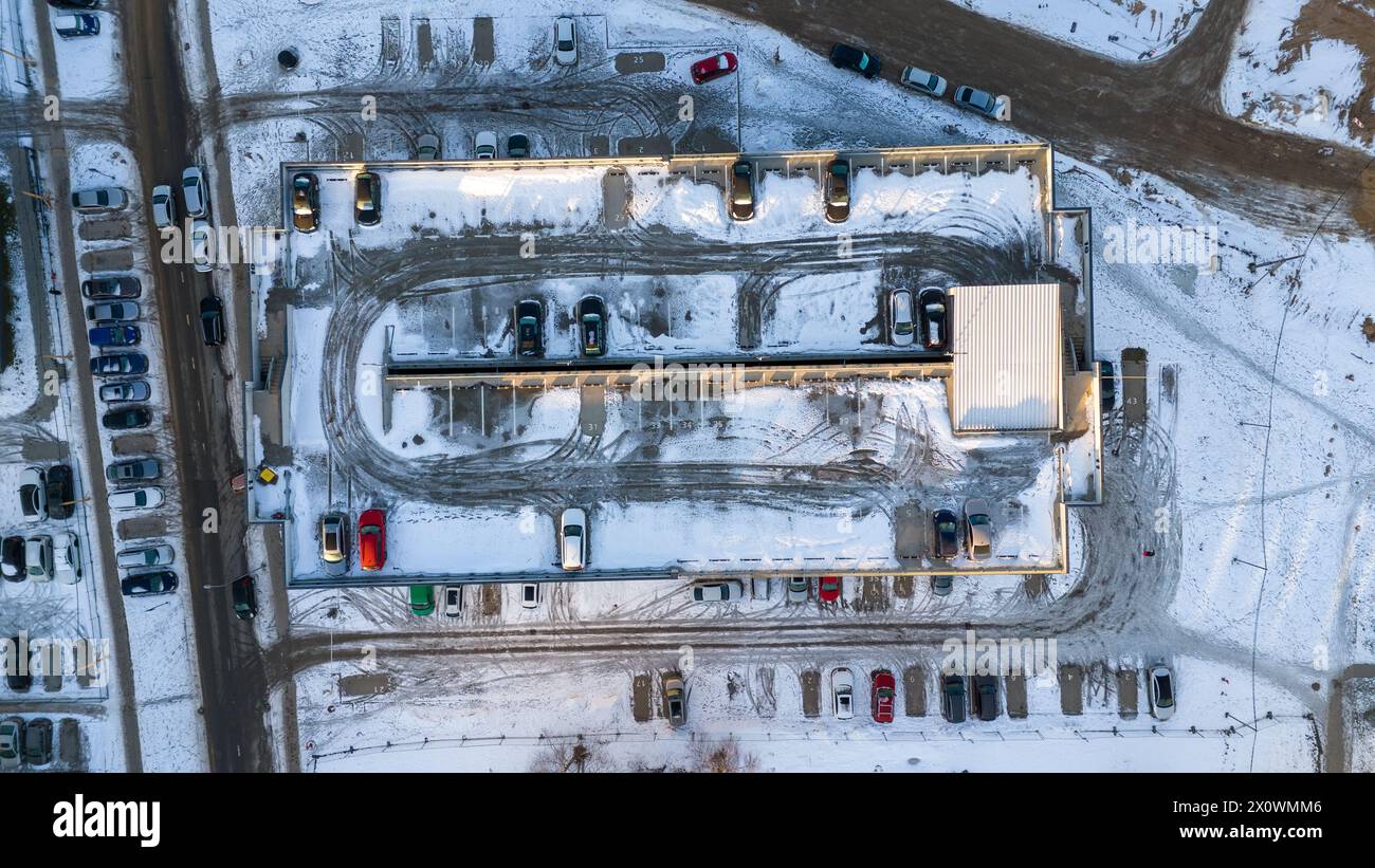 Drohnenfotografie von oben nach unten auf einen mehrstöckigen Parkplatz mit ein paar Autos und bedeckt von Schnee an sonnigen Wintertagen Stockfoto