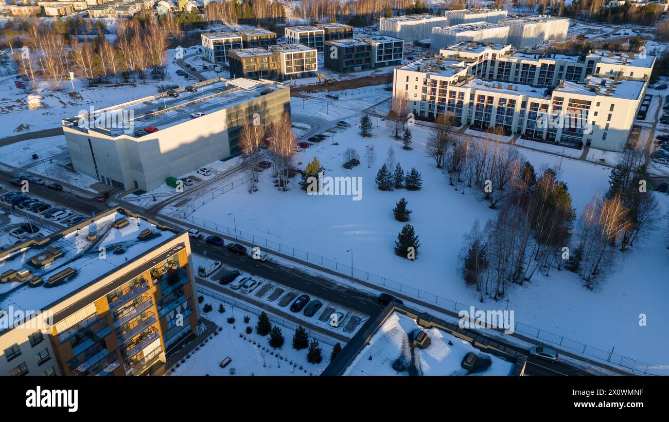 Drohnenfotografie von einigen mehrstöckigen Häusern, mehrstöckigem Parkplatz, schneebedecktem Park und einer Baustelle für einen Wohnblock während des Winters sunn Stockfoto