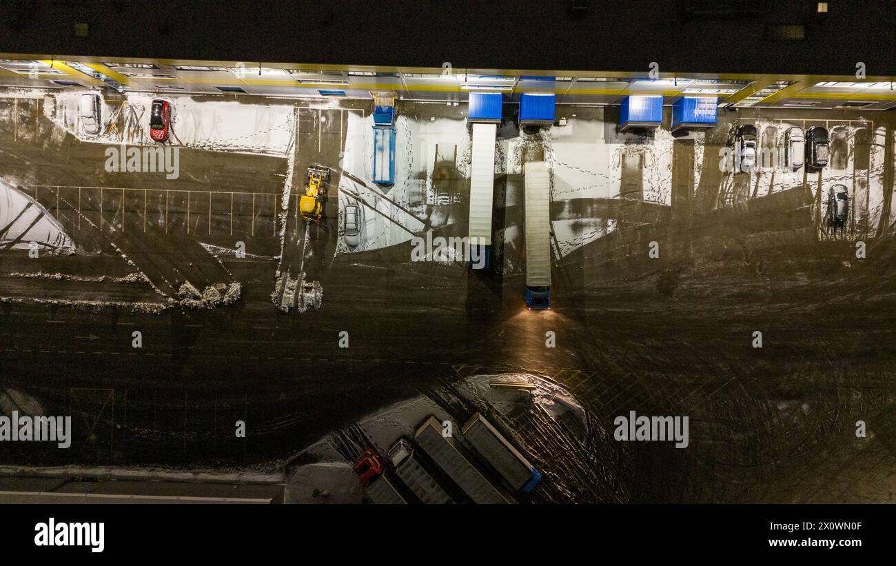 Drohnenfotografie von Logistiklagern und geparkten LKWs während der winterlichen bewölkten Nacht Stockfoto