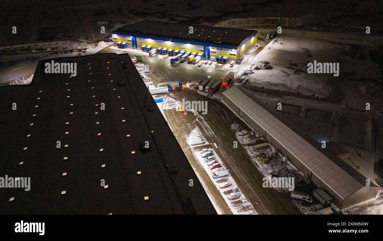 Drohnenfotografie von Logistiklagern und geparkten LKWs während der winterlichen bewölkten Nacht Stockfoto