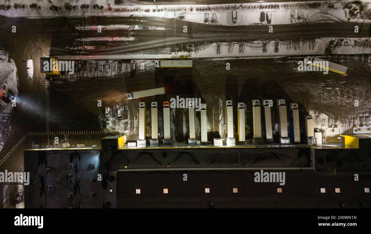 Drohnenfotografie von Logistiklagern und geparkten LKWs während der winterlichen bewölkten Nacht Stockfoto