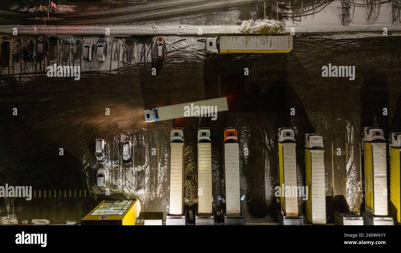 Drohnenfotografie von Logistiklagern und geparkten LKWs während der winterlichen bewölkten Nacht Stockfoto