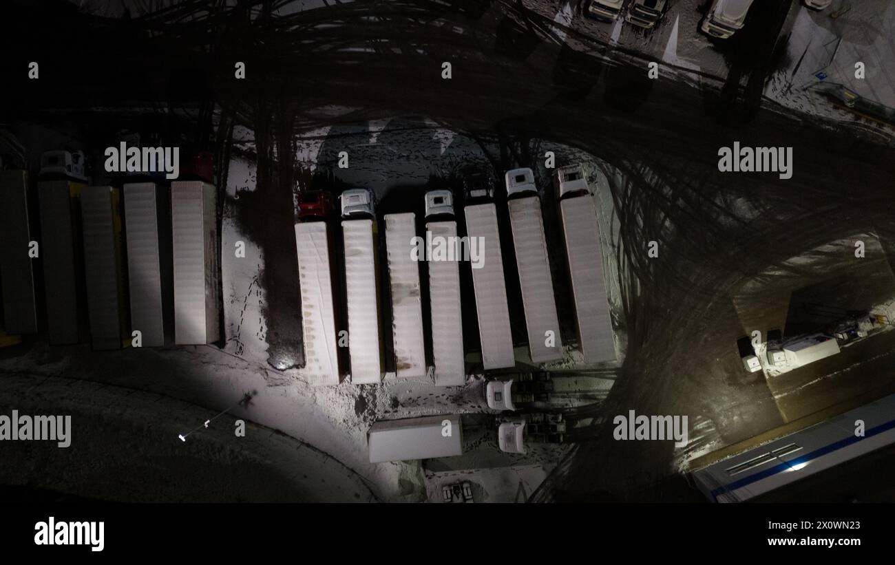 Drohnenfotografie von Logistiklagern und geparkten LKWs während der winterlichen bewölkten Nacht Stockfoto