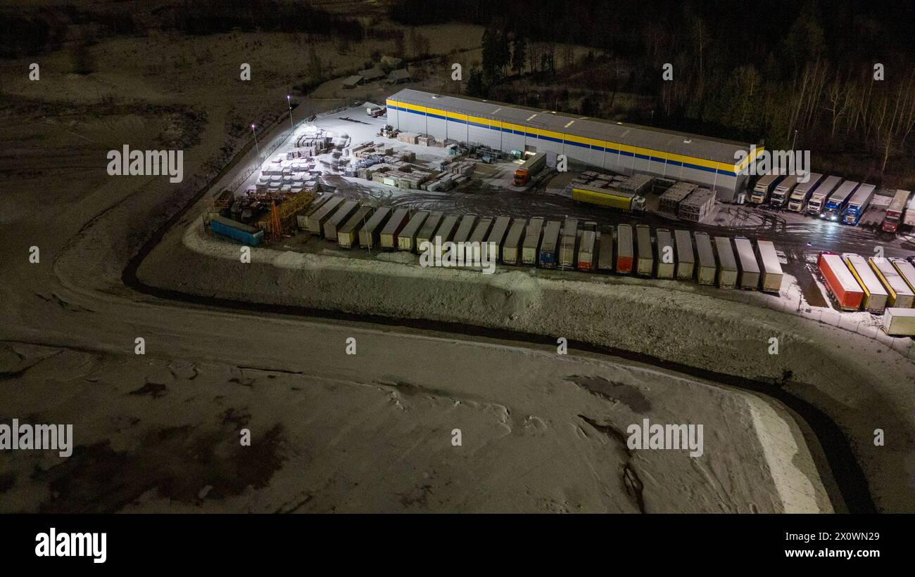 Drohnenfotografie von Logistiklagern und geparkten LKWs während der winterlichen bewölkten Nacht Stockfoto