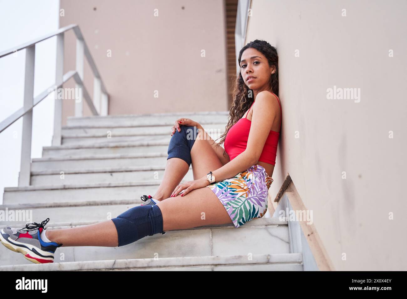 Junge Latina, die auf der Treppe sitzt und auf die Kamera blickt Stockfoto