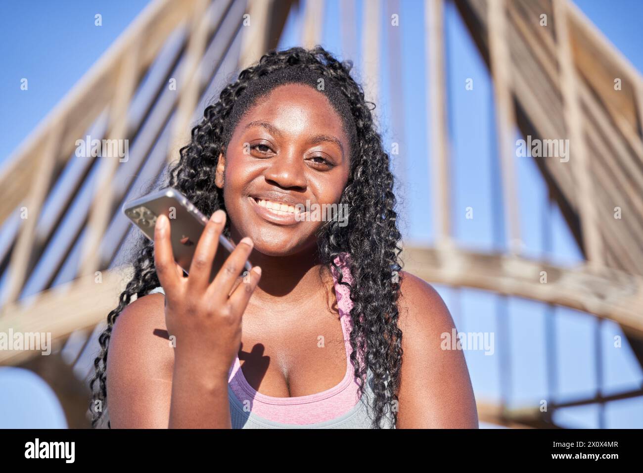 Porträt einer jungen afroamerikanischen Frau, die mit einem Smartphone in der Hand lächelt Stockfoto