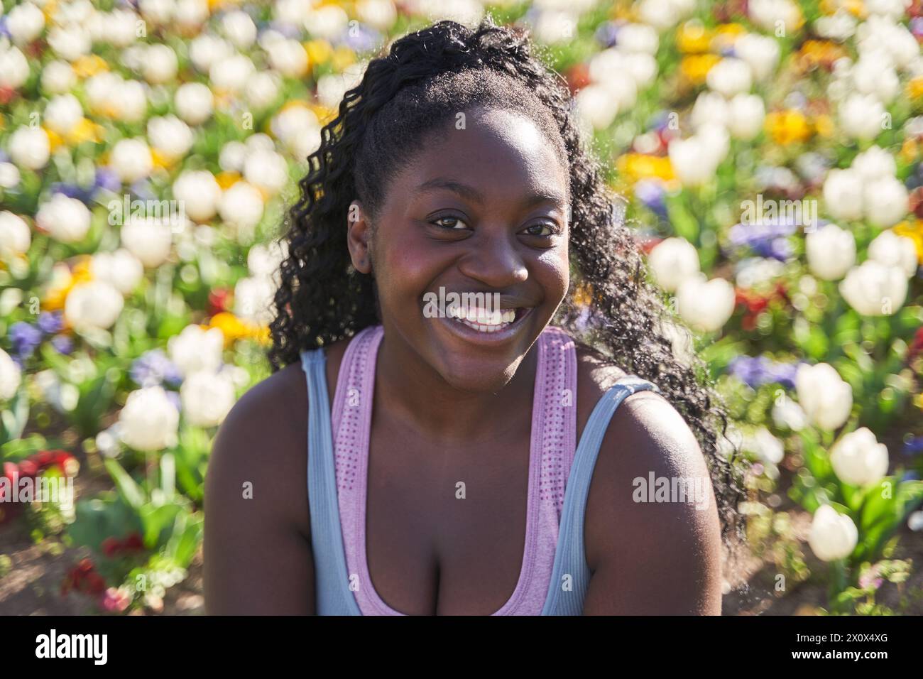 Porträt einer afroamerikanischen Frau in einer Umgebung voller bunter Blumen Stockfoto