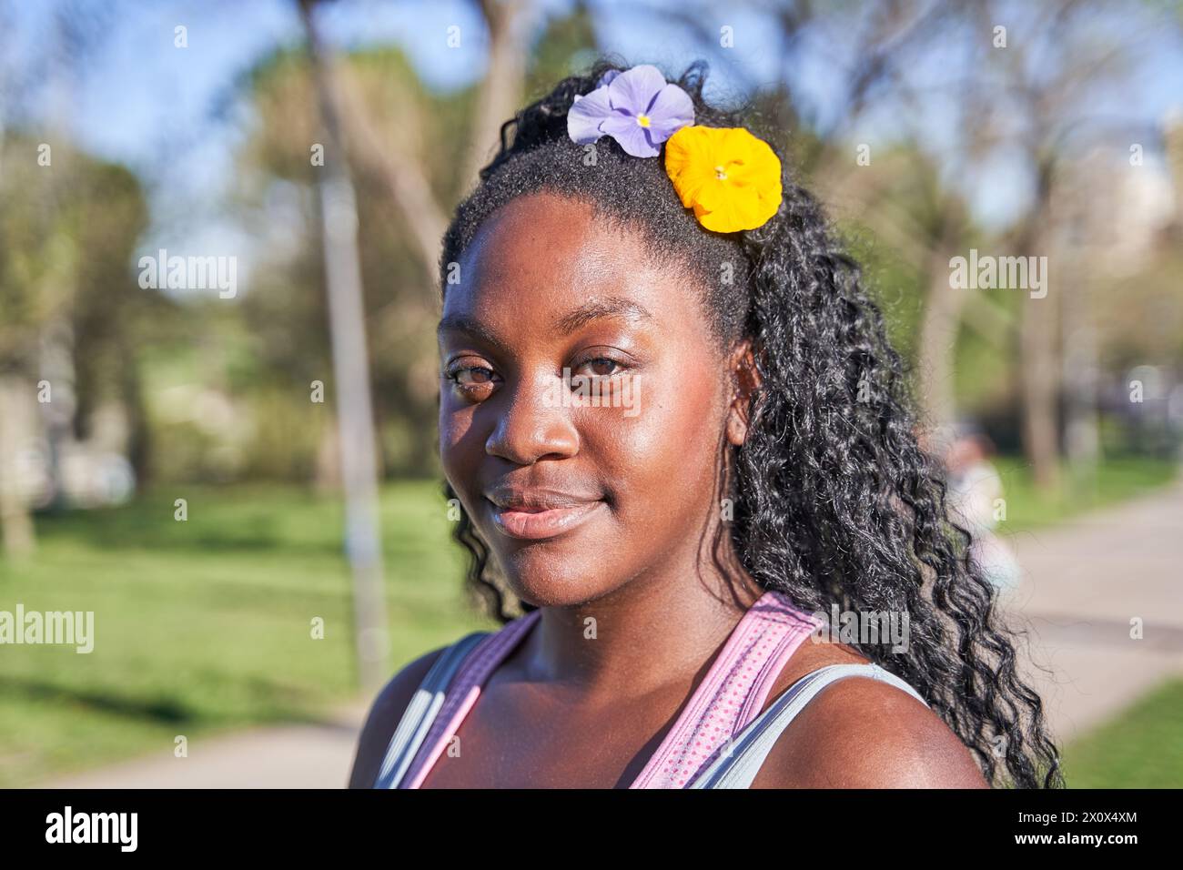 Nahporträt einer afroamerikanischen Frau, die mit Blumen in den Haaren in die Kamera schaut Stockfoto