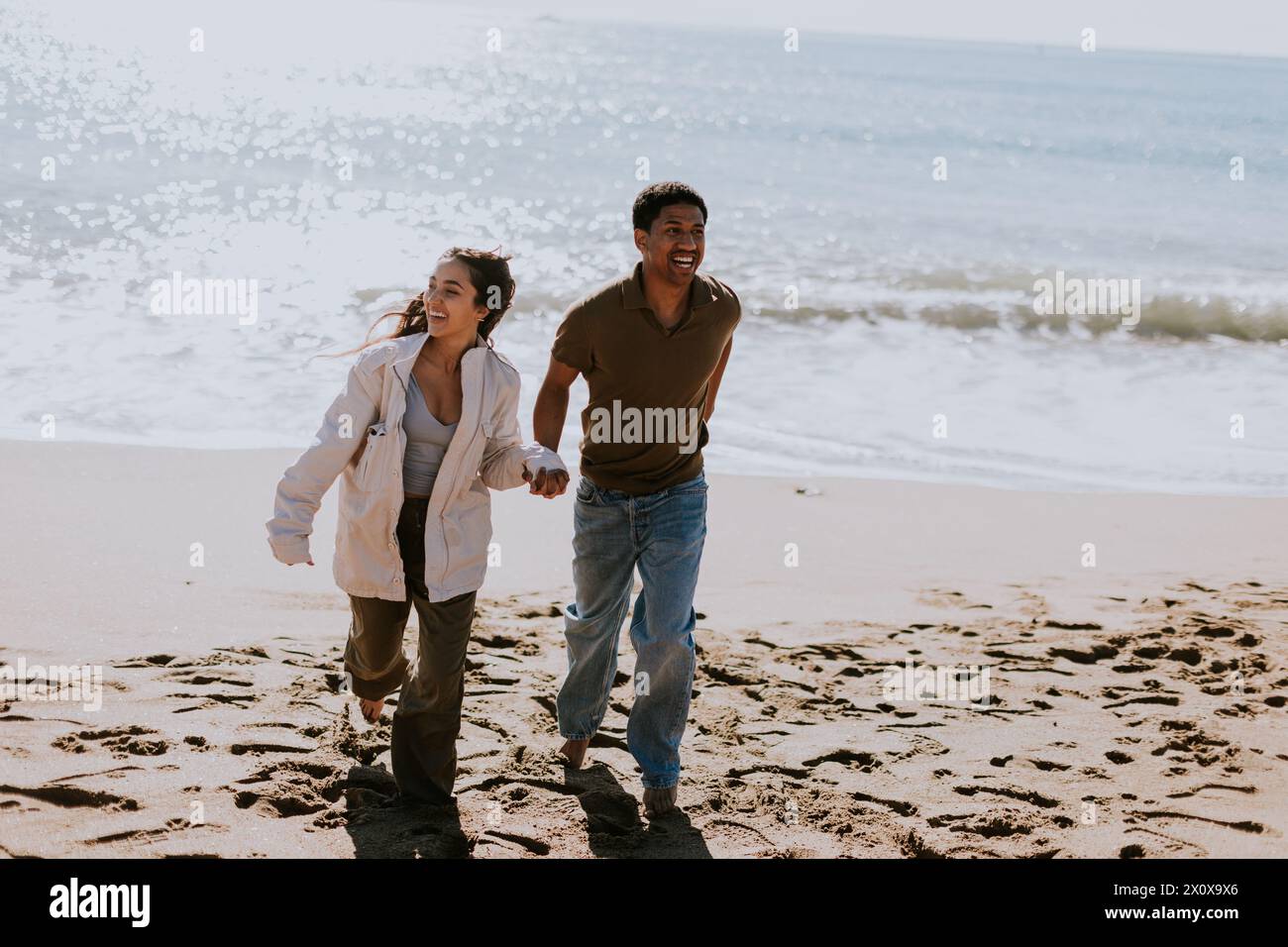 Ein lächelndes Paar genießt einen sorglosen Lauf an einem Sandstrand, Wellen brechen sanft in den Hintergrund Stockfoto