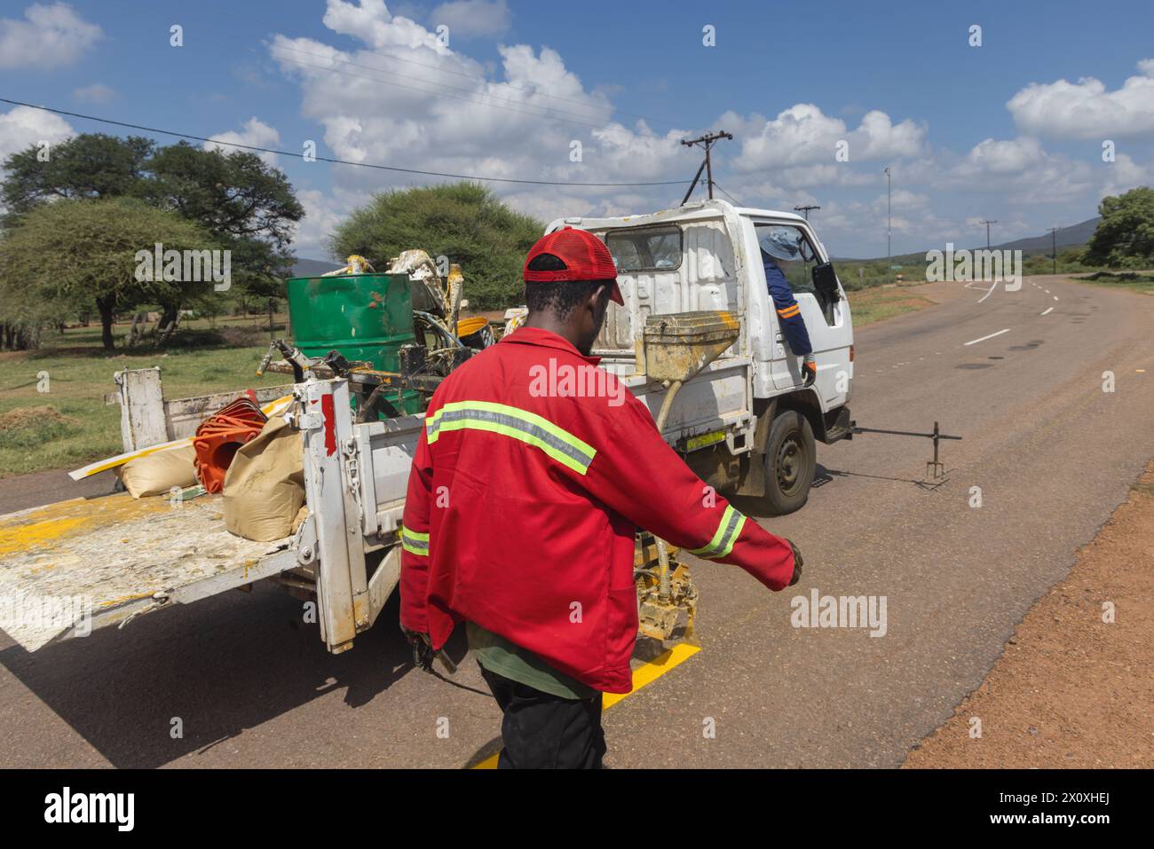 afrikanische Männer reparieren und pflegen verblasste Straßenmarkierungen auf der Autobahn, streichen gelbe Markierungen für die Verkehrssicherheit neu Stockfoto