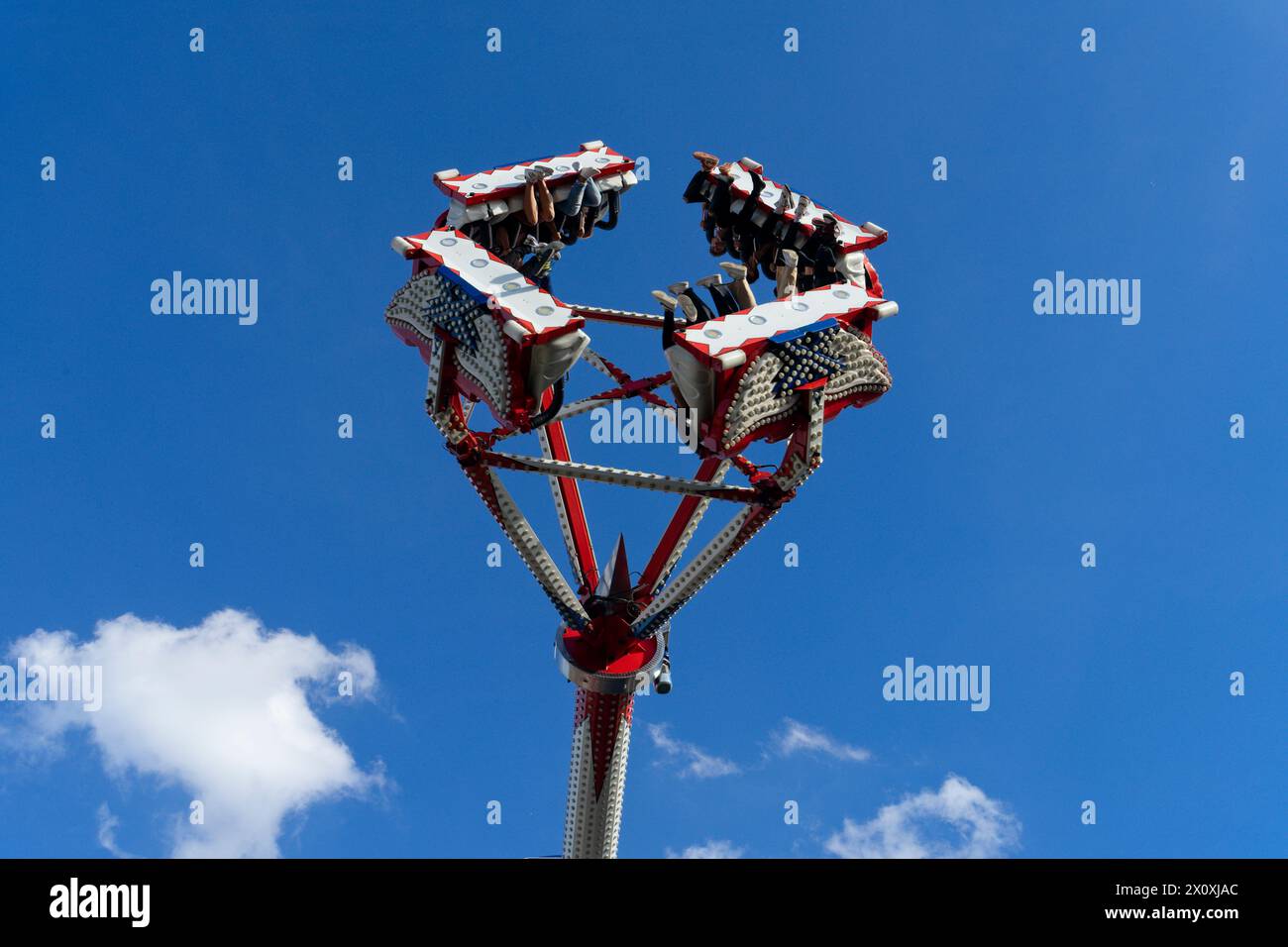 Ein Vergnügungspark mit Nervenkitzel suchenden Menschen, die hoch in einen blauen Himmel mit flauschigen Wolken fliegen. Eine urkomische, frei fallende Turmfahrt bei einem Countr Stockfoto