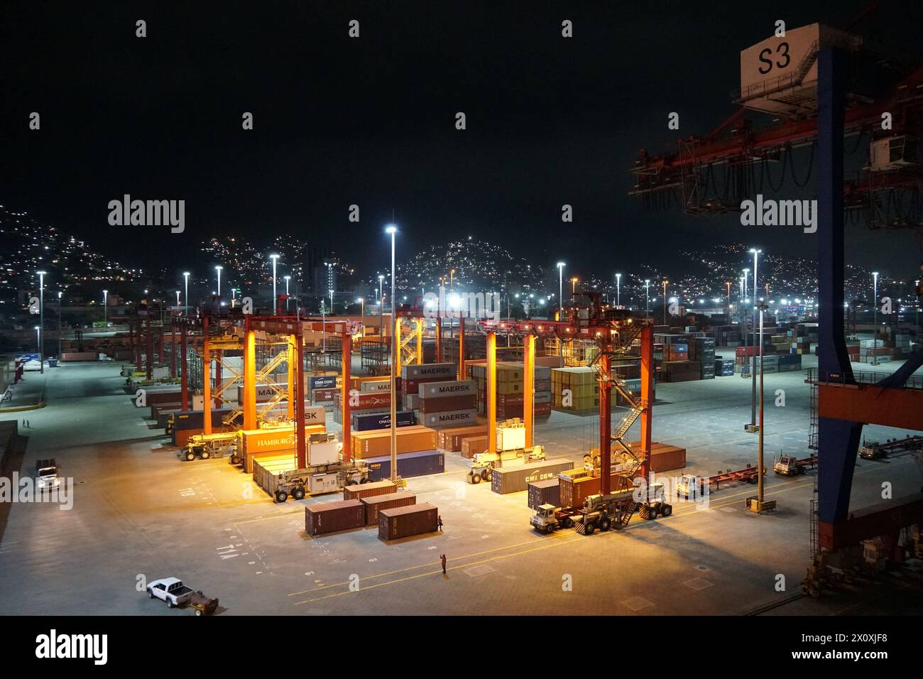 Moderner Containerterminal während des Nachthafens von La Guairá, beobachtet von einem Frachtschiff, das unter Portalkranen verankert ist. Stockfoto