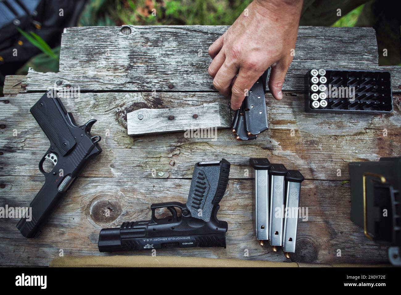 Dallas, Texas, USA - 07. April 2024: Handfeuerwaffen und Munition auf einem Tisch mit der Hand eines weißen kaukasischen Mannes, der eine Zeitschrift aufnimmt Stockfoto