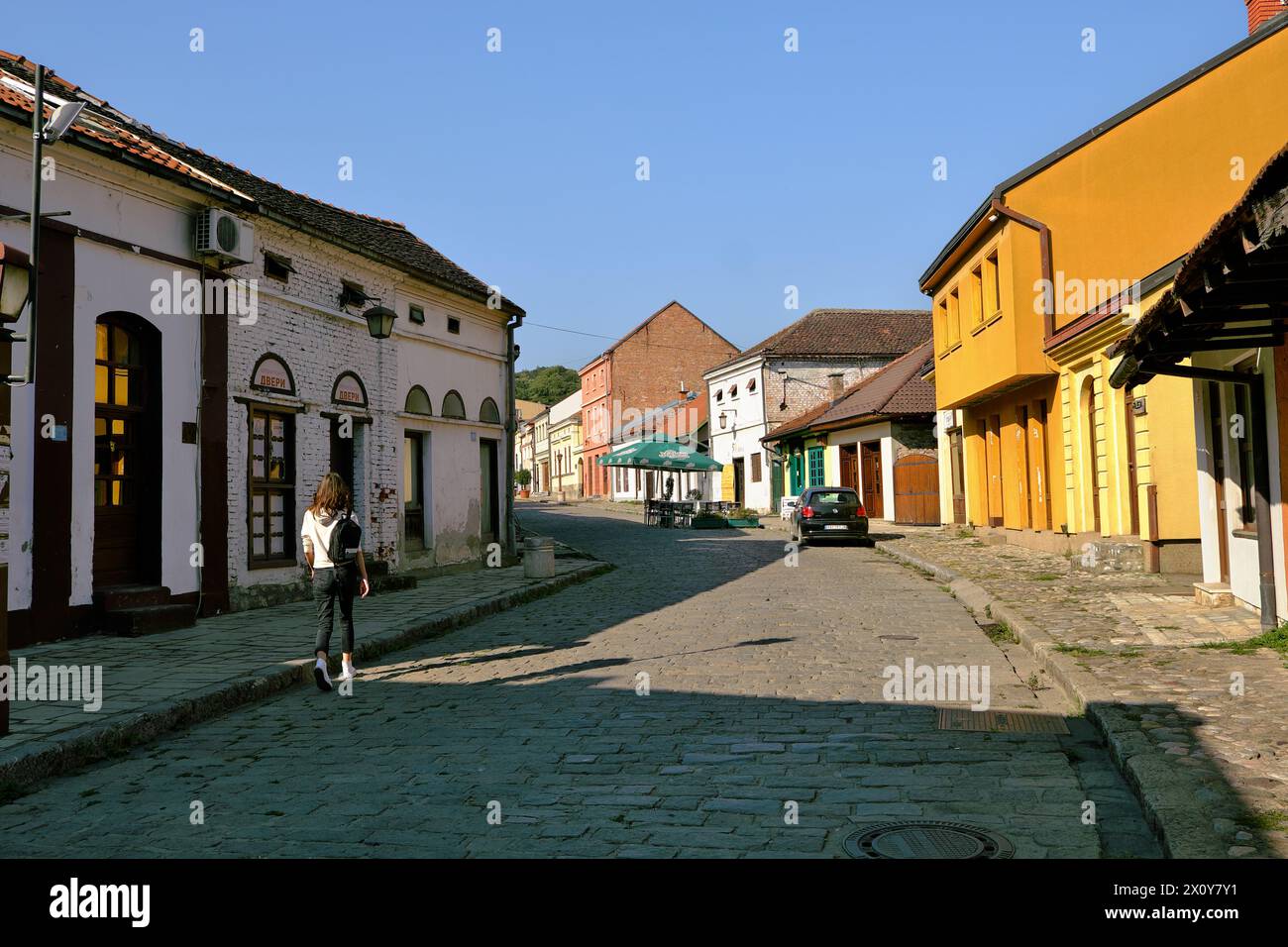 Eine allein stehende junge Frau, die auf einer Kopfsteinpflasterstraße zwischen den Geschäften und Geschäften läuft, die auf dem Tesnjar-Basar in Valjevo, Serbien, geschlossen sind Stockfoto