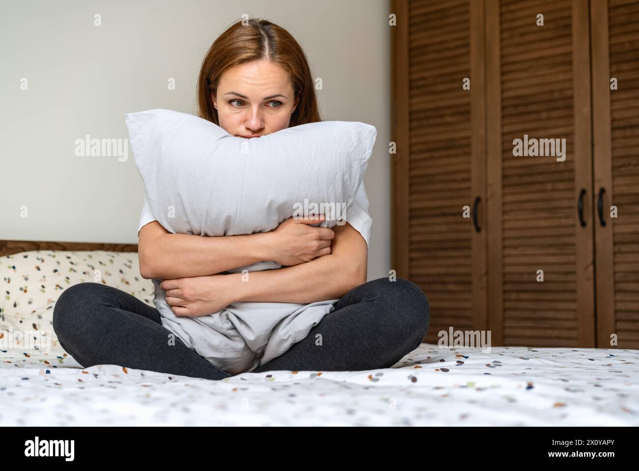 Einsame Frau sitzt auf dem Bett im Schlafzimmer und umarmt Kissen. Depressive Frau mit leerem Ausdruck. Stockfoto