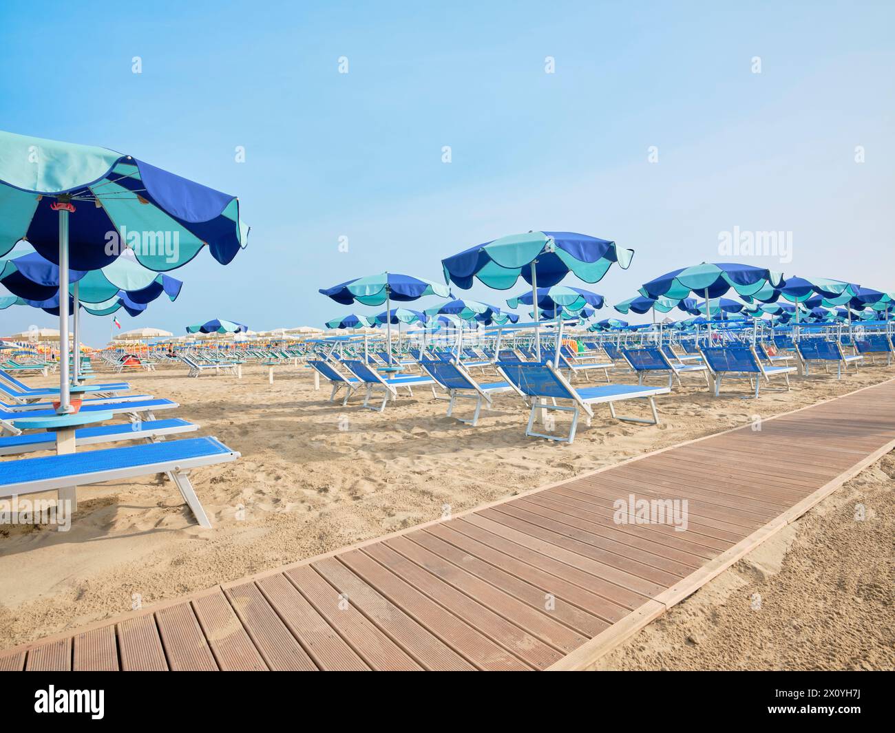 Strandpromenade am Strand entlang einer Reihe von bunten Sonnenschirmen und Liegen, die an einem sonnigen Sommertag am Ufer der Adria, Italien, zum Meer führen. Stockfoto