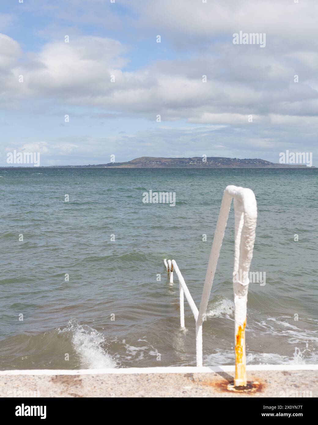 Untergetauchte Geländer und Stufen im Meer am Seapoint in Irland. Howth ist im Hintergrund Stockfoto