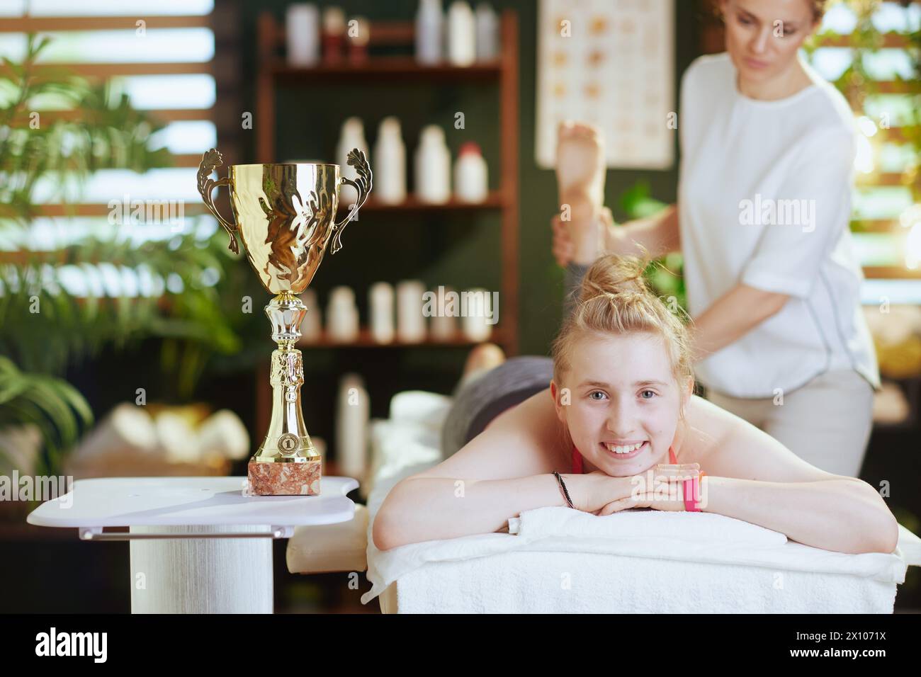 Gesundheitszeit. Weibliche medizinische Massage-Therapeutin in Massageschrank mit Klemmbrett, Teenager-Klientin und Award Cup Make Massage. Stockfoto