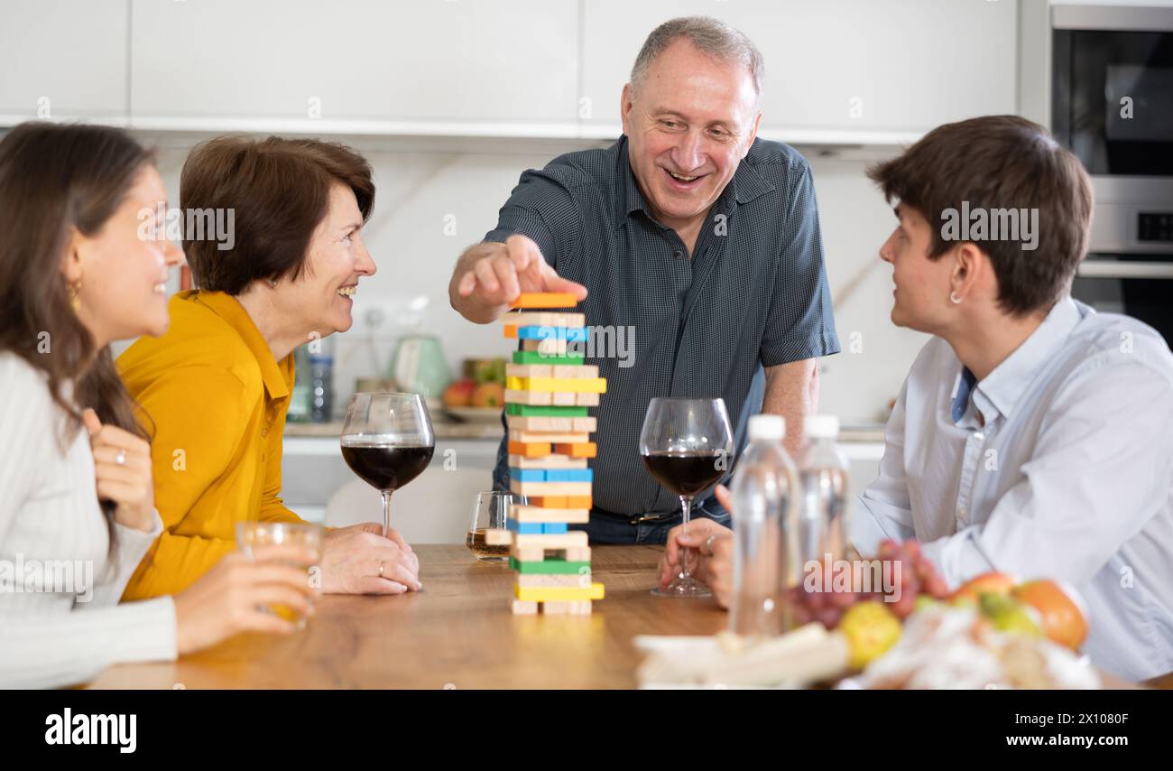 Lächelnder älterer Mann oder Vater, der Spaß beim Turmbau mit Frau und erwachsenen Kindern in einem komfortablen Familienhaus hat Stockfoto