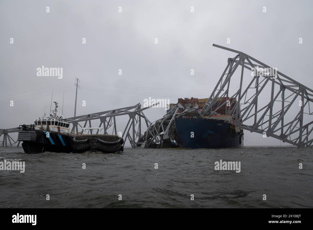 Dundalk, Vereinigte Staaten von Amerika. April 2024. Ein Bergungsschiff greift auf den Schaden des verwickelten Frachtträgers MV Dali zu, der in den Stahlträgern der eingestürzten Francis Scott Key Bridge, die den Kanal Fort McHenry blockiert, am 3. April 2024 in der Nähe von Dundalk, Maryland, eingehüllt ist. Die Brücke wurde am 26. März von einem 984-Fuß-Containerschiff getroffen und stürzte zusammen, wobei sechs Arbeiter ums Leben kamen. Quelle: PO2 Alejandro Rivera/US Coast Guard/Alamy Live News Stockfoto