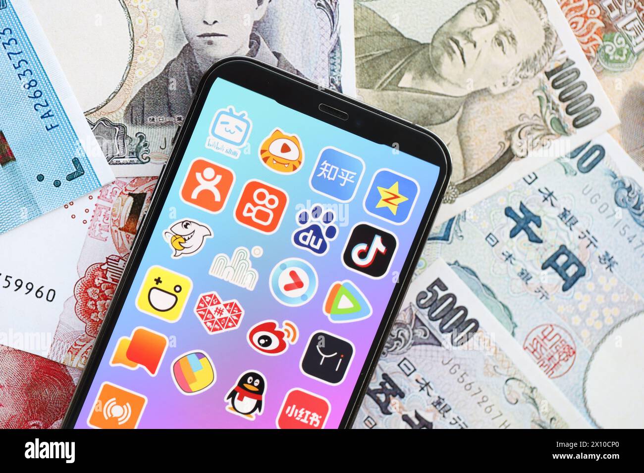 KIEW, UKRAINE - 1. APRIL 2024 Symbol für asiatische Apps auf dem Smartphone-Bildschirm auf vielen asiatischen Geldrechnungen. IPhone-Display mit App-Logo mit japanischen Yen- und chinesischen Yuan-Banknoten Stockfoto