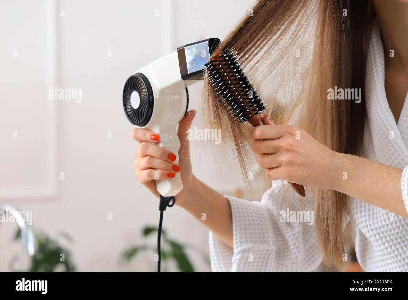 Schöne Frau, die ihr Haar mit runder Bürste im Badezimmer trocknet, Nahaufnahme Stockfoto