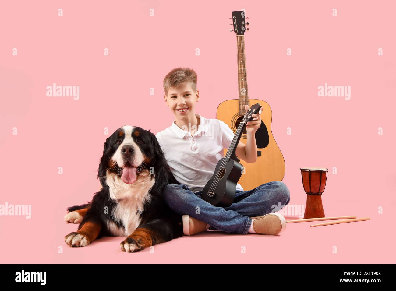 Kleiner Junge mit Berner Berghund und Musikinstrumenten auf rosa Hintergrund Stockfoto