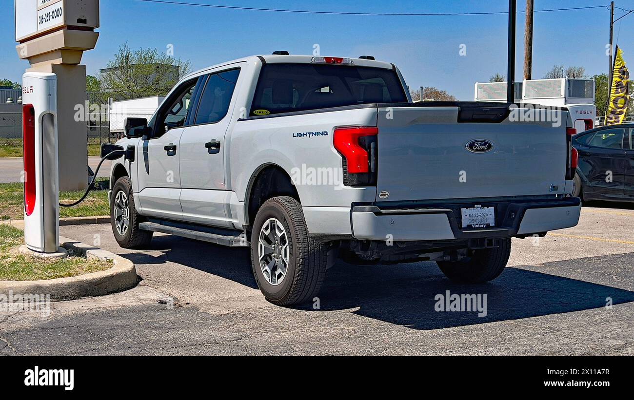 EMPORIA, KANSAS- 14. APRIL 2024 Ein kürzlich gekaufter Ford F150 komplett elektrischer Lightning Pickup-Truck wird an eine Tesla Supercharger Station auf dem Parkplatz des Emporia West Shopping plaza angeschlossen. Stockfoto