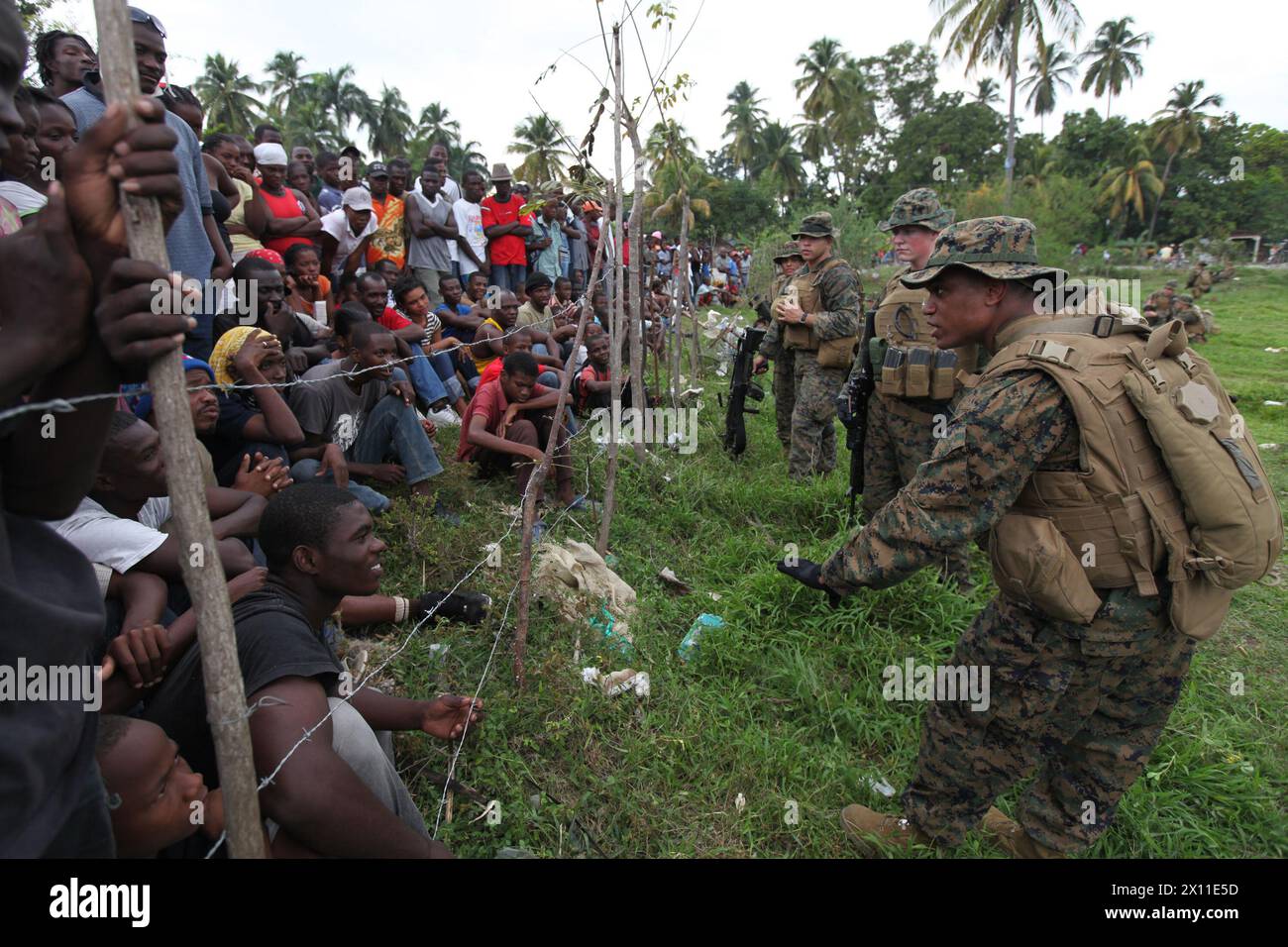 CPL. Clifford Sajous, ein Teamleiter und Linguist mit dem Battalion Landing Team, 3rd Battalion, 2nd Marine Regiment, 22nd Marine Expeditionary Unit, übersetzt, wie er und andere Marines mit lokalen Haitianern interagieren, während einer Mission zur Versorgung mit Nahrungsmitteln und Wasser in Leogane am 20. Januar 2010. Stockfoto