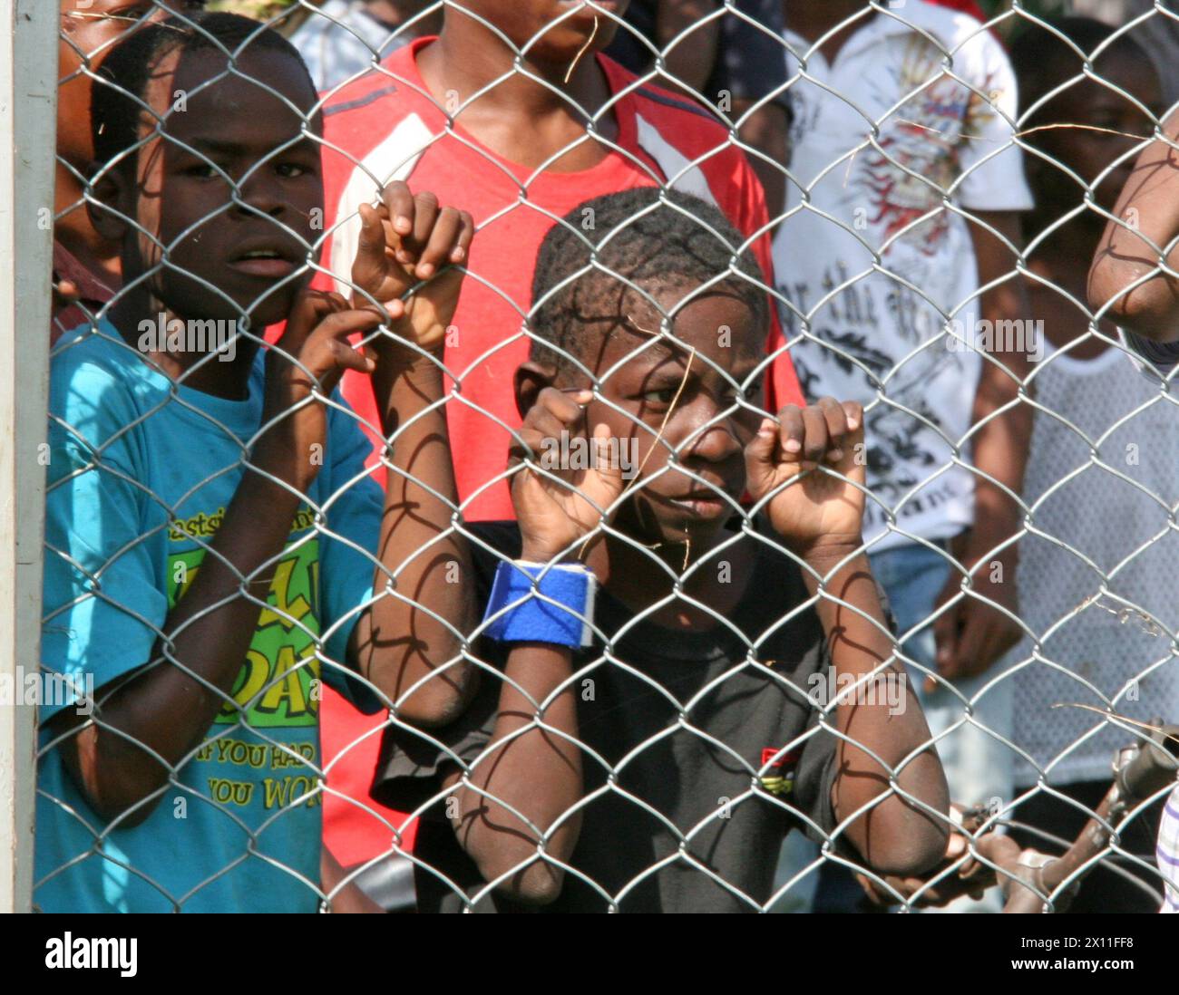 Haitianische Kinder beobachten durch einen Zaun, wie Marines der India Company, des Battalion Landing Teams, des 3. Bataillons, des 2. Marine Regiments, der 22. Marine Expeditionary Unit, eine Landezone in Petit Goave, Haiti, 24. Januar 2010, sichern. Als Reaktion auf ein verheerendes Erdbeben, das das Land Haiti heimsuchte, begannen Marines und Seeleute der 22. MEU, Hilfsgüter zu liefern und medizinische Hilfe zur Unterstützung der Operation Unified Response am 19. Januar zu leisten. Stockfoto