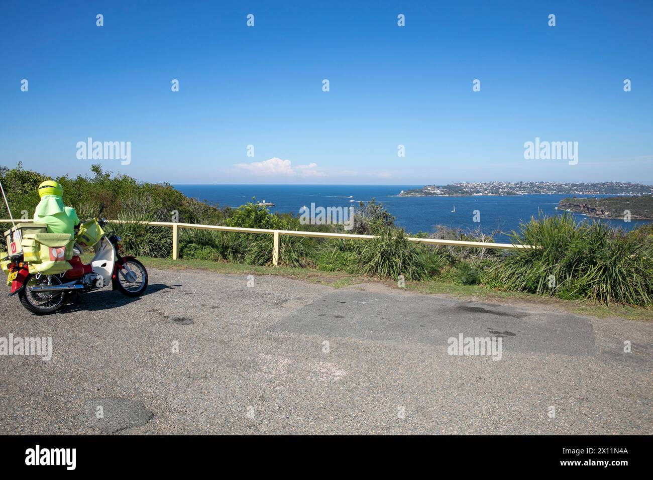 Australische Postman Postie in Sydney auf einer Pause mit Honda Motorrad genießt Blick auf den Hafen von Sydney von Dobroyd Head, Sydney, NSW, Australien Stockfoto