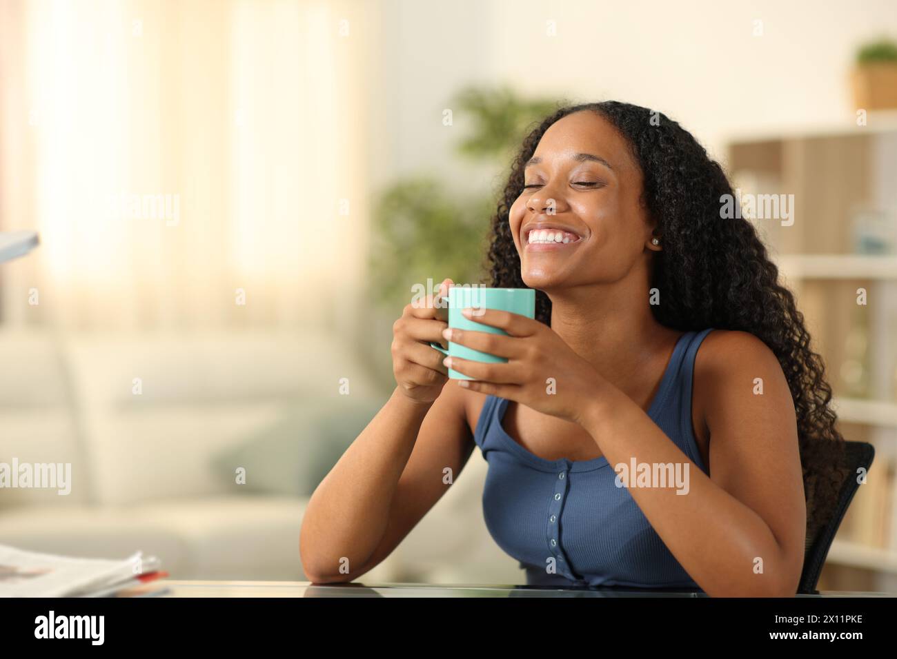 Glückliche schwarze Frau genießt den Geruch von Kaffee und lächelt zu Hause Stockfoto