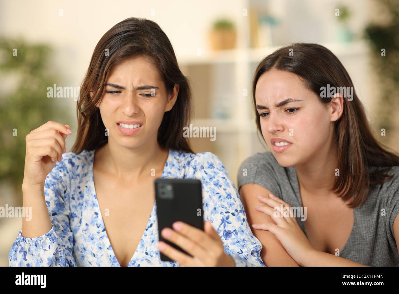 Zwei Freunde sehen sich zu Hause auf dem Telefon unangenehme Inhalte an Stockfoto