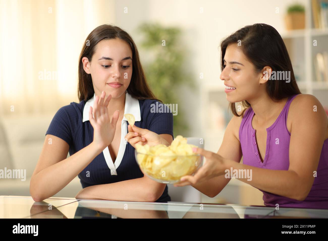 Frau, die einem Freund Kartoffelchips anbietet, der es zu Hause ablehnt Stockfoto