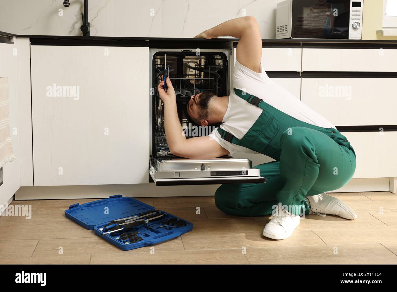 Service repariert Geschirrspüler mit Schraubendreher in der Küche Stockfoto