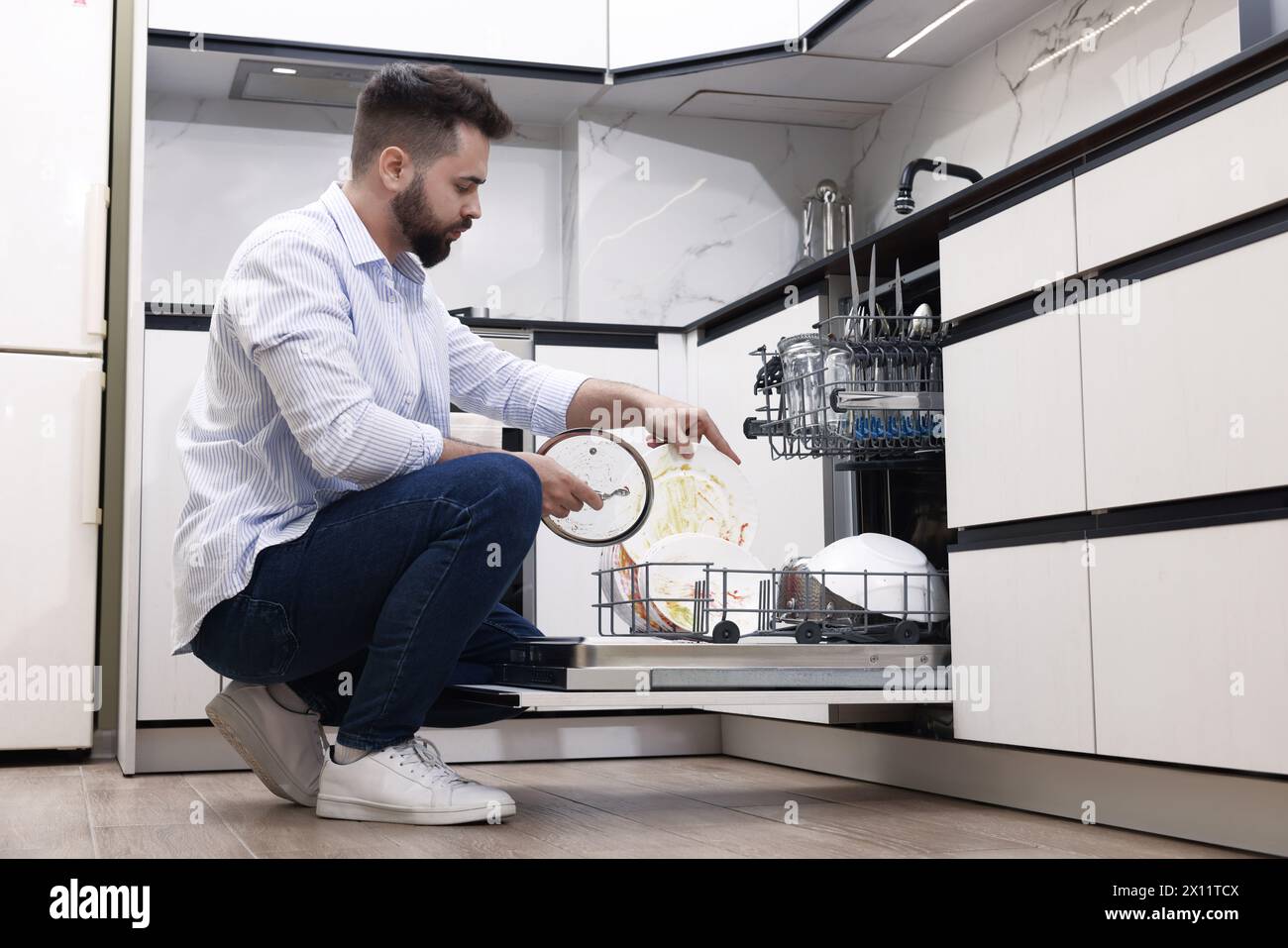 Mann, der in Innenräumen Geschirrspüler mit schmutzigen Tellern lädt Stockfoto