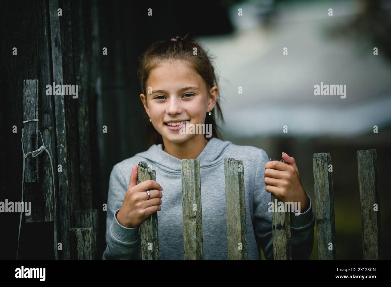 Ein Teenager steht hinter einem hölzernen Zaun, ihr Blick nach vorne gerichtet, sie sieht besinnlich und träumerisch aus. Stockfoto