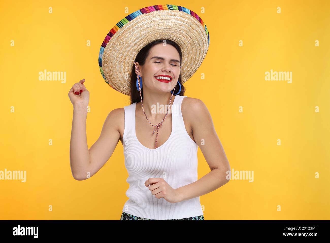 Junge Frau mit mexikanischem Sombrero-Hut, der auf gelbem Hintergrund tanzt Stockfoto