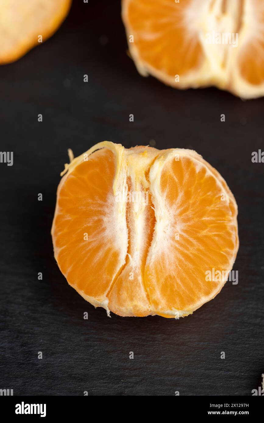 Geschält, Orangen-Mandarinen auf dem Tisch in Nahaufnahme, eine große Anzahl von Orangen-Zitrusfrüchten auf einer schwarzen Schieferoberfläche Stockfoto