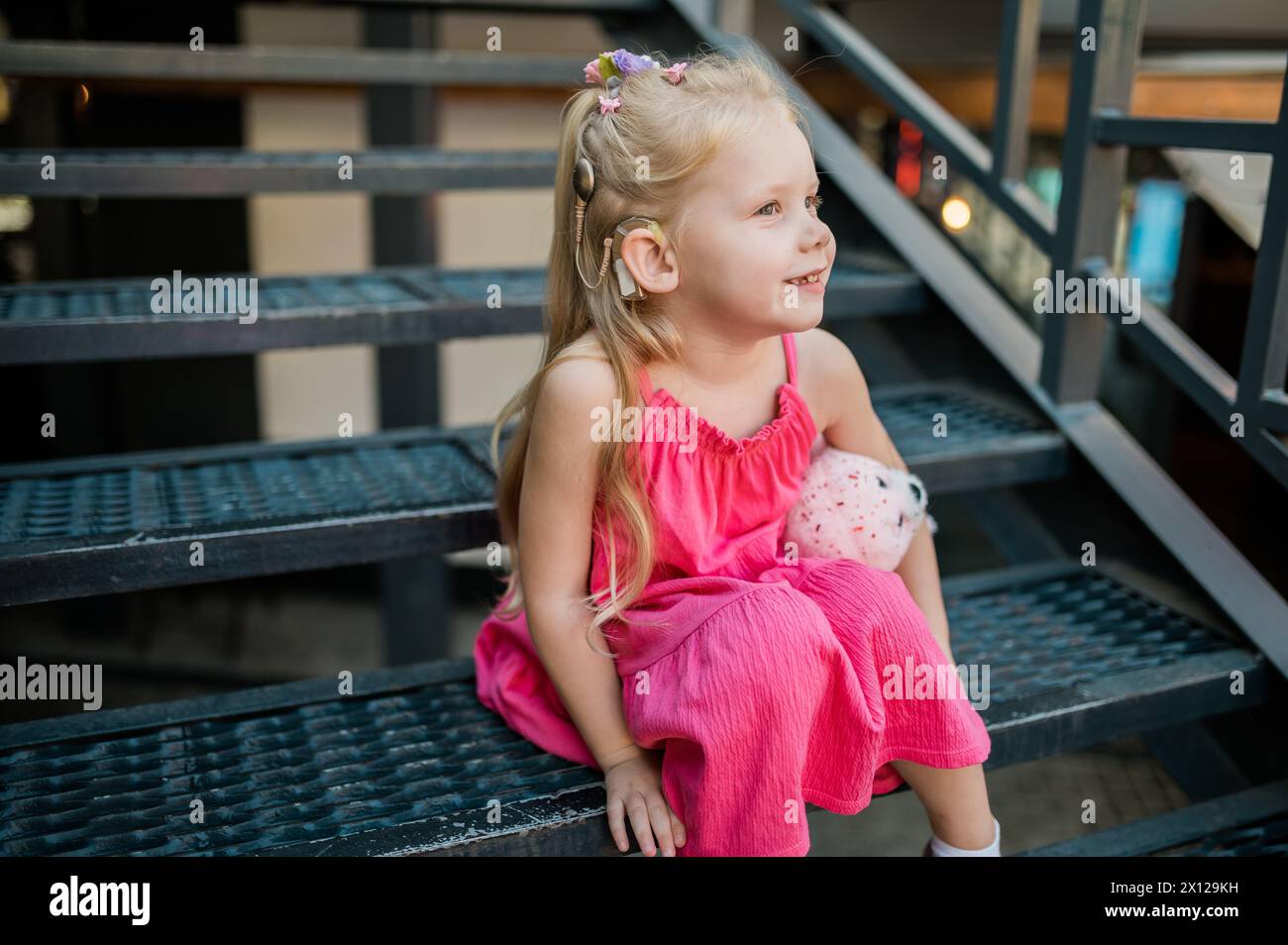 Kindermädchen mit Hörgerät und Cochlea-Implantationssystem. Kind mit Hörproblemen geht im Sommer im Freien. Inklusion und Diversität Stockfoto