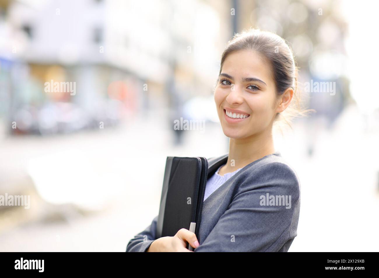 Glücklicher Manager, der einen Ordner hält, der auf der Straße posiert und dich ansieht Stockfoto