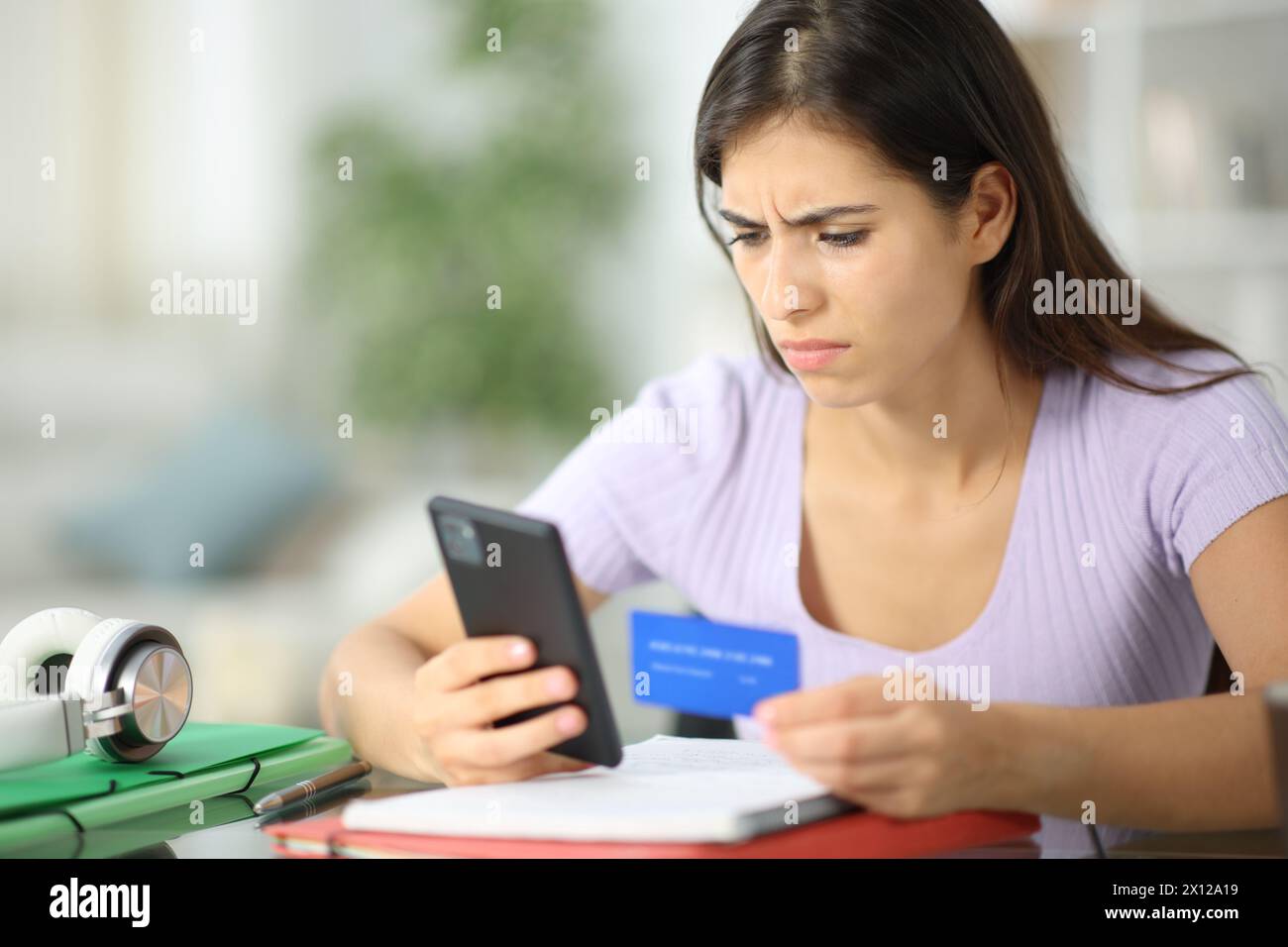 Besorgter Student, der zu Hause online mit Kreditkarte und Telefon kauft Stockfoto