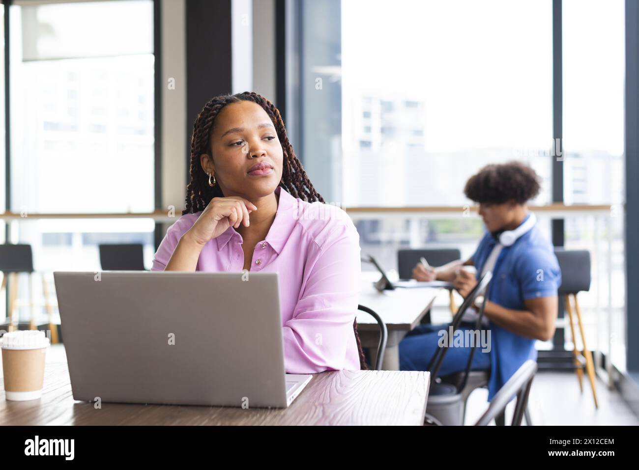 Eine junge Frau mit geflochtenen Haaren arbeitet in einem modernen Geschäftsbüro an einem Laptop Stockfoto