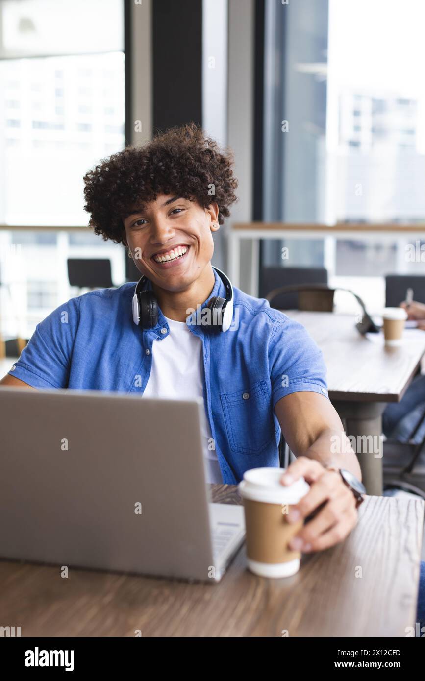 Ein junger, birassischer Mann mit lockigen braunen Haaren arbeitet in einem modernen Geschäftsbüro an einem Laptop Stockfoto