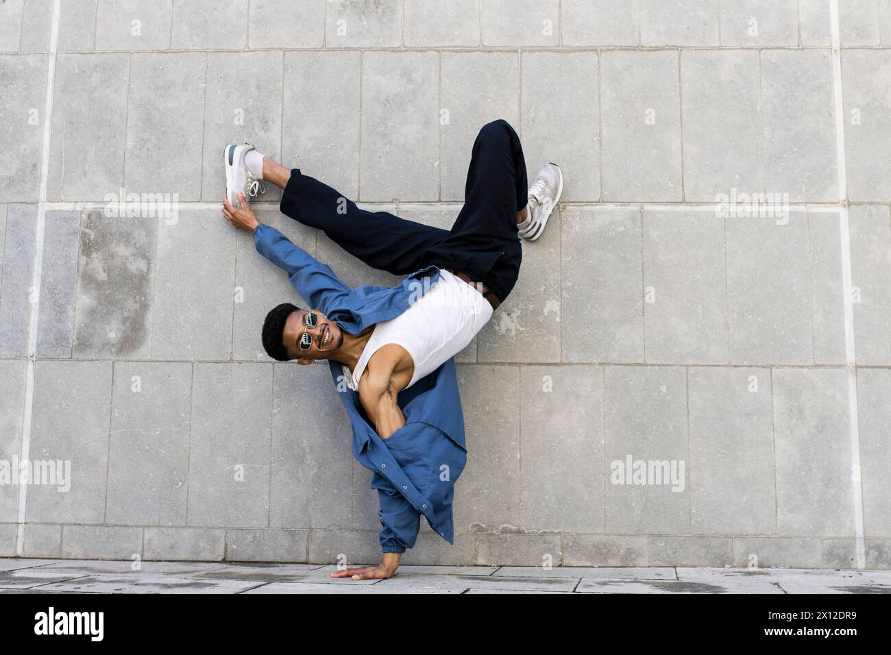 Junge coole männliche Tänzerin, die Breakdance auf Stadtmauern-Hintergrund spielt. Stockfoto