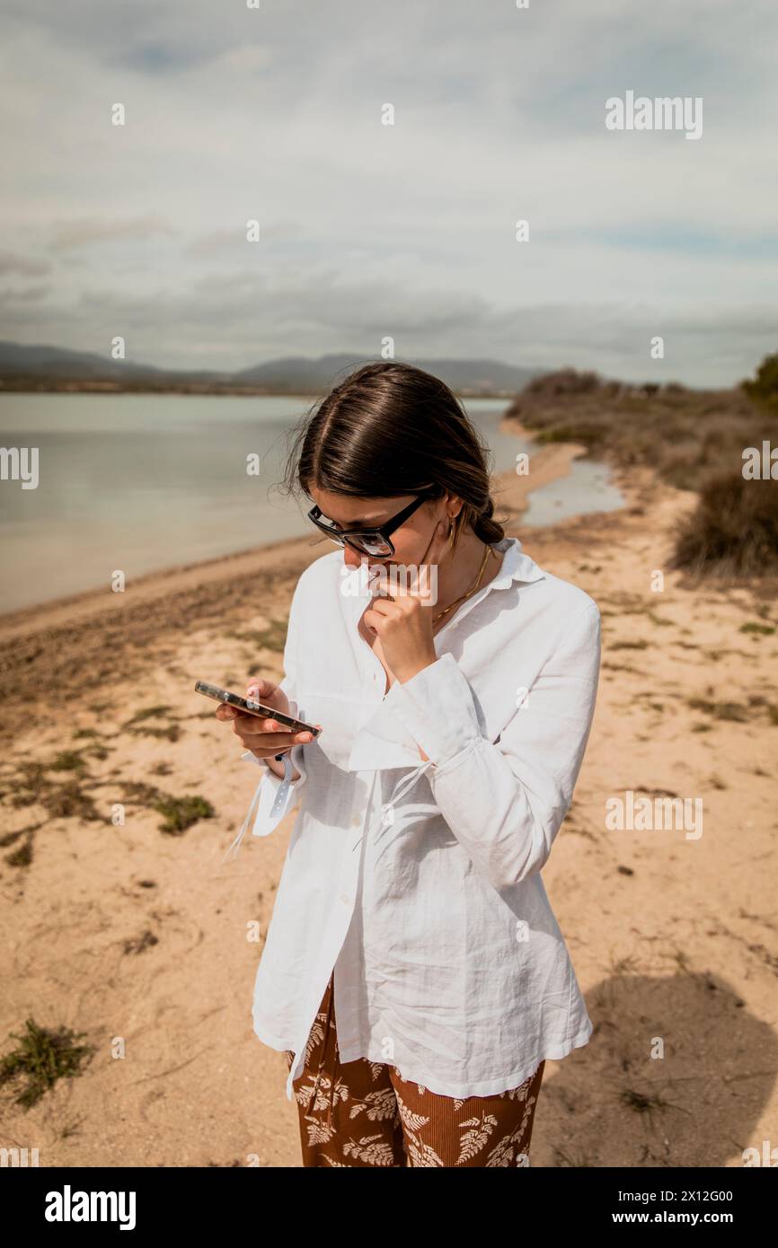 Mädchen in einem weißen Hemd und einer Sonnenbrille, die auf ihrem Smartphone schreibt Stockfoto